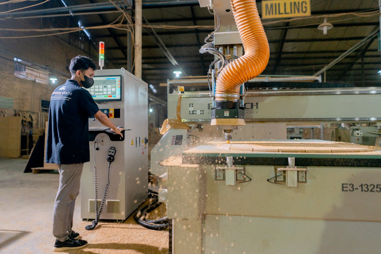 An industrial worker oversees a milling machine in a busy factory environment.